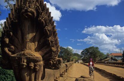 Una mujer pedalea por el Spean Praptos, el puente más impresionante de la ruta de los puentes angkorianos, con gigantescas ‘nagas’ (cobras) de piedra que amparan la imagen de Buda.