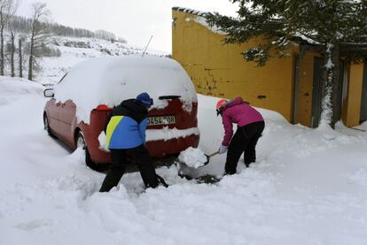 Dos jóvenes retiran con una pala la nieve acumulada alrededor de su coche en el municipio leonés de Puebla de Lillo.