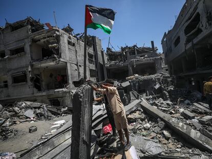 Varias personas izan una bandera palestina junto a su casa destruida tras un ataque aéreo israelí en el campo de refugiados de Bureij, en el sur de la franja de Gaza, el martes.