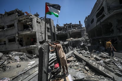Varias personas izan una bandera palestina junto a su casa destruida tras un ataque aéreo israelí en el campo de refugiados de Bureij, en el sur de la franja de Gaza, el martes.