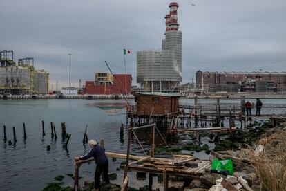 Un hombre pesca en el pequeño muelle de una caseta de pescadores locales frente al puerto industrial y comercial de Rávena.