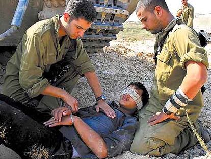 Dos soldados israelíes comprueban el estado de un palestino al que acaban de hacer prisionero en el norte de la franja de Gaza.
