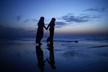 Un par de niñas palestinas caminan tomadas de la mano al atardecer en la playa de la ciudad de Gaza, en Palestina.