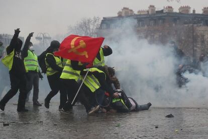 Unos 'chalecos amarillos' ayudan a un herido por el cañón de agua durante la protesta, cerca del Arco del Triunfo
