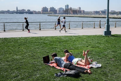 People read a book and use a laptop sunbathing on the Hudson river banks in Manhattan, New York on April 23, 2025