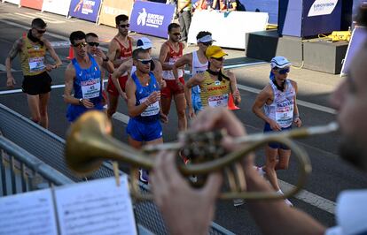 Los atletas pasan junto a una banda de música mientras compiten en la carrera.