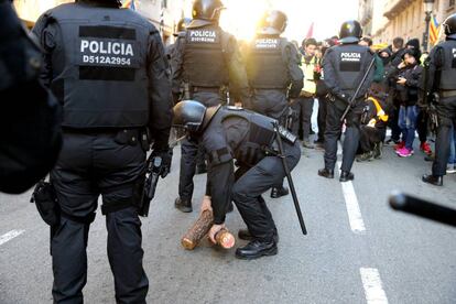 Un 'mosso' recoge dos leños que representan a 'tió de Nadal' durante la marcha por la Vía Laietana de Barcelona.