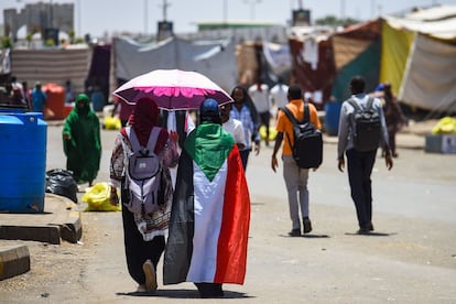 Una mujer sudanesa camina envuelta en una bandera nacional junto a otra manifestante durante una protesta frente a la sede del ejército en la capital, Jartum.