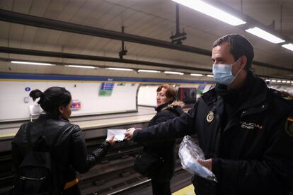 Un agente de policía ofrece mascarillas de protección contra el coronavirus entre los usuarios del transporte público en una estación del metro madrileño, este lunes.