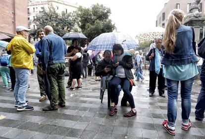 Una pareja se resguarda de la lluvia mientras miran sus teléfonos móviles.