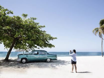 Una mujer fotograf&iacute;a un coche antiguo en una playa de Cuba. 
