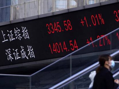 Una persona con mascarilla sube por unas escaleras junto a unos paneles con la cotización de la Bolsa de Shangai.