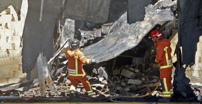 Dos bomberos entre los restos de la nave incendiada en Museros.