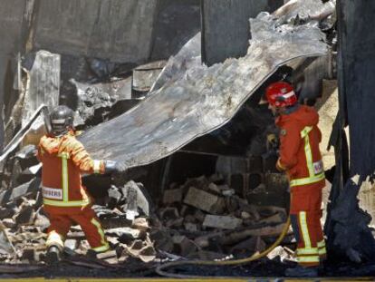 Dos bomberos entre los restos de la nave incendiada en Museros.