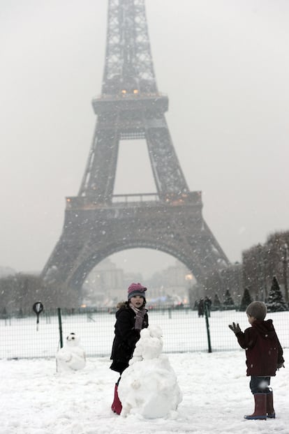 Unos niños hacen un muñeco de nieve frente a la Torre Eiffel.