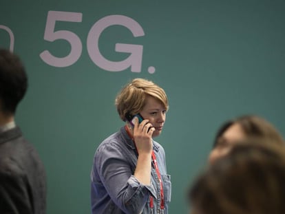 Una mujer camina mientras habla por telefono mientras pasa junto a un anuncio de tecnologia 5G.
