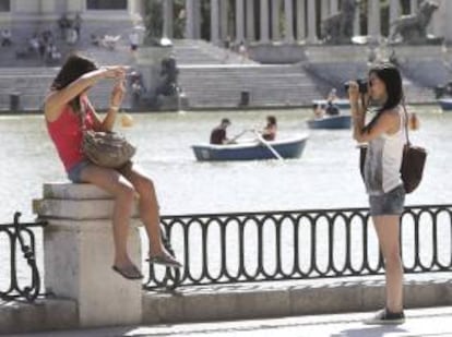 Dos turistas se fotografían en el parque del Retiro mientras otros pasean en barca. EFE/Archivo