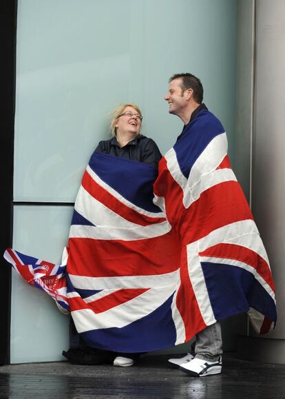 Una pareja espera protegi&eacute;ndose de la lluvia con una bandera cerca de Tower Brigde.