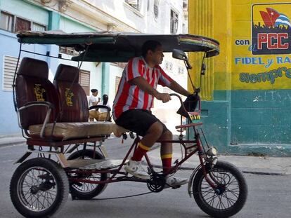 Un hombre conduce un bicitaxi frente a un cartel alusivo el Partido Comunista de Cuba (PCC), en La Habana (Cuba).