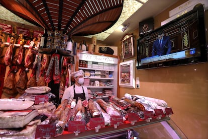 Un comerciante de una charcuteria del mercado de La Paz, en Madrid, escucha la comparecencia del presidente del Gobierno, Pedro Sánchez.