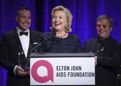Hillary Clinton tras recibir el premio de la Fundación Elton John. Detrás, el cantante y su marido, David Furnish.