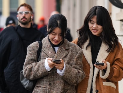 Two women walk while looking at their cell phones during Milan Fashion Week in January.