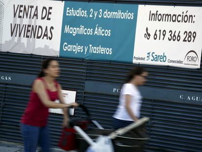 Dos mujeres pasan ante un anuncio de venta de viviendas de la Sareb, en una imagen de archivo.