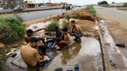 Jóvenes aseándose en un charco en una carretera de Caracas (Venezuela).