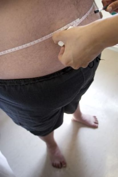Un paciente obeso se mide la cintura en la consulta de un m&eacute;dico.
