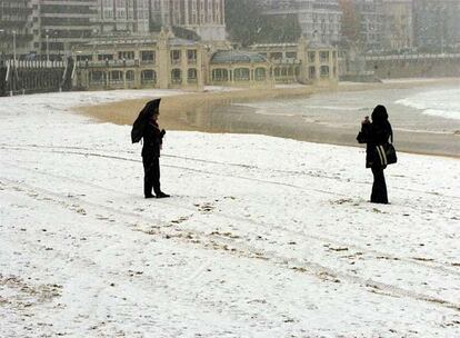 No es frecuente hollar la playa de la Concha con un manto de nieve, así que los turistas se aprestan a fotografiarse.