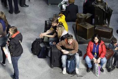 Varios afectados por la huelga de Renfe, sentados en la estación madrileña de Atocha.