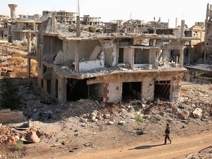 Um rebelde caminha em frente a construções destruídas na parte rebelde de Deraa.