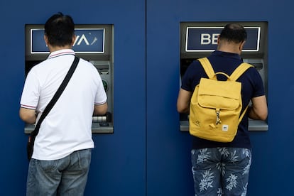 Dos hombres sacan dinero del cajero en una oficina bancaria del BBVA, en Gran Vía, Madrid.