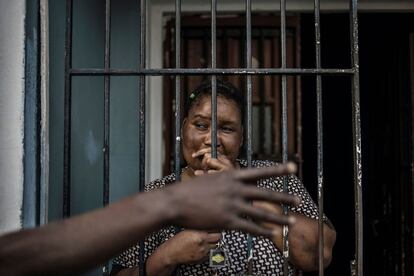 Una mujer zimbabuense mira a través de la reja de su ventana mientras charla con otro vecino.