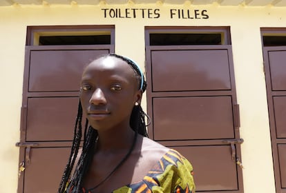 La estudiante, Bintou Dieme, de 14 años, posa frente a los baños de su colegio bajo el letrero 'toilettes filles' (aseos chicas). 