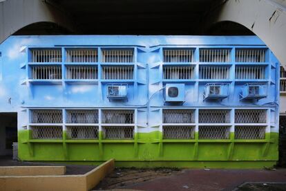 Fachada de vigas metálicas pintadas de azul y verde tras las que se encuentra un refugio antiaéreo.