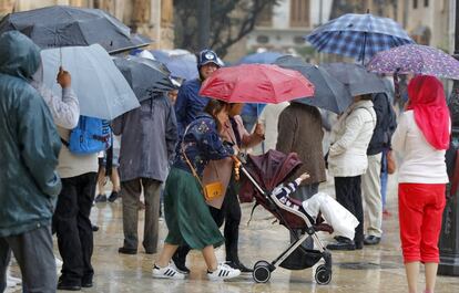Dos mujeres, con un carrito de bebé, se resguardan de las lluvias en Valencia bajo un paraguas.