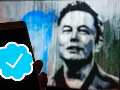 Un móvil muestra el controvertido símbolo de verificación de pago de Twitter, que Elon Musk (al fondo en una pintada en Bruselas, Bélgica) implantó a su llegada a la plataforma.