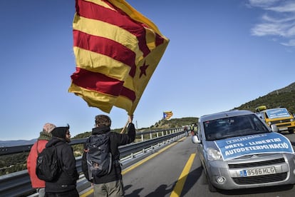 Manifestants amb una estelada davant de cotxes amb cartells del Tsunami Democràtic.