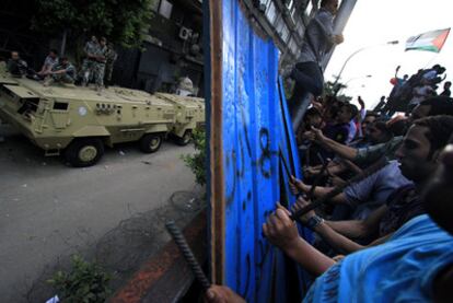 Soldados egipcios protegen la Embajada de Israel, ayer en El Cairo. En frente, los manifestantes hacen ruido con barras de hierro para protestar por la muerte de militares egipcios en el Sinaí.