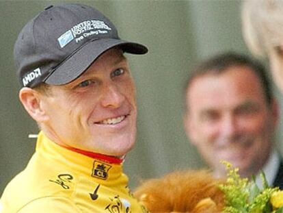 Lance Armstrong, en el podio tras enfundarse el jersey amarillo de líder y, al fondo, el pentacampeón de la ronda Bernard Hinault.