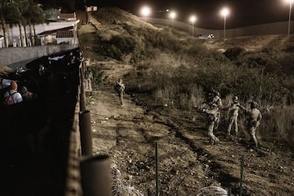 Oficiales de Protección Fronteriza de los Estados Unidos apuntan con sus armas a los migrantes mientras se preparaban para cruzar la valla para ingresar a San Diego, California, desde Tijuana, México.
