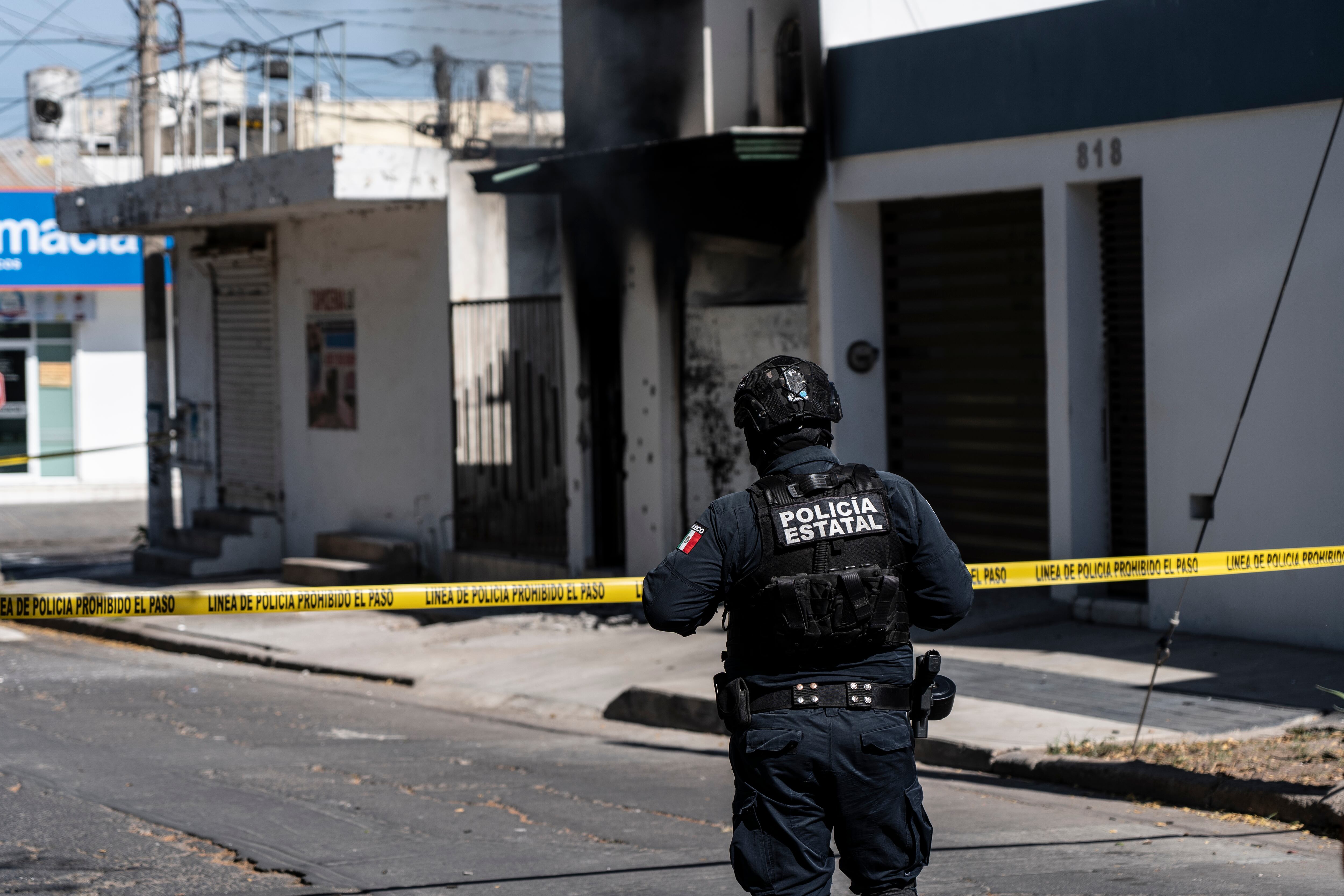 Un policía estatal resguarda la zona donde una casa fue quemada y atacada a balazos en Culiacán.