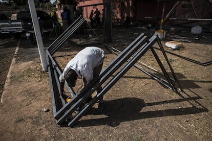 Ao outro lado do campo, onde uma árvore proporciona uma sombra generosa, saltam faíscas de onde operários cortam e soldam metais. Estão construindo traves para gol.