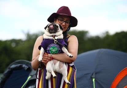 Una asistente al torneo coge a su perro, vestido con el atuendo de Wimbledon antes del inicio del campeonato.