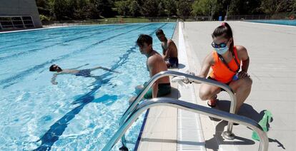 La socorrista de las piscinas de Aranzadi de Pamplona desinfecta la escalera de acceso mientras un grupo de jóvenes toman el sol o disfrutan del baño.