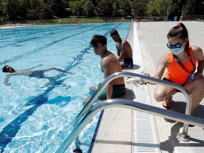 La socorrista de las piscinas de Aranzadi de Pamplona desinfecta la escalera de acceso mientras un grupo de jóvenes toman el sol o disfrutan del baño.
