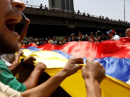 Manifestantes contrários a Maduro erguem bandeira da Venezuela.