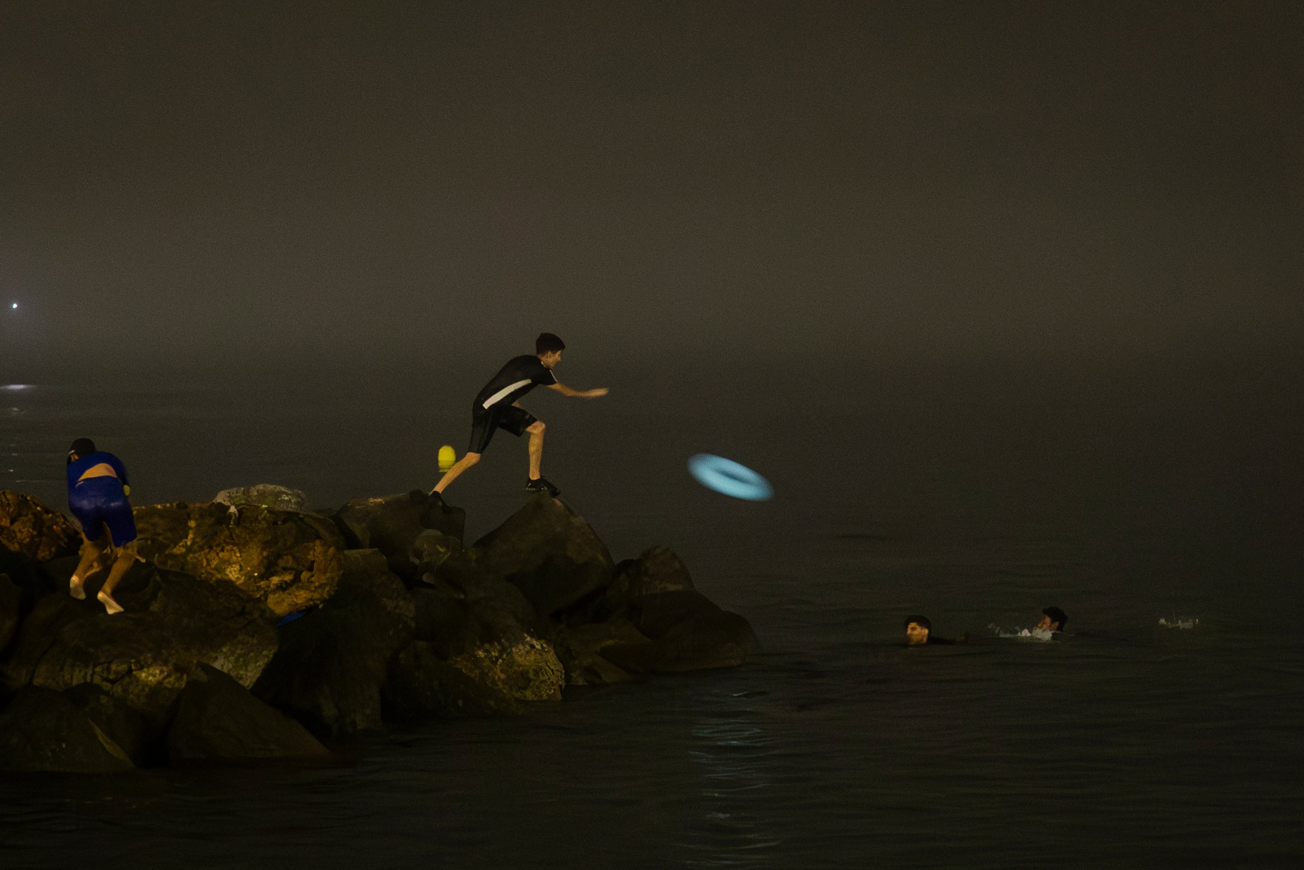 Un joven arroja un flotador a varios compañeros de travesía mientras intentan alcanzar la playa de El Tarajal en la madrugada del viernes al sábado. 