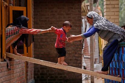 Dos mujeres ayudan a un niño a cruzar a otra casa tras las inundaciones  repentinas en Tailbal, en las afueras de Srinagar.